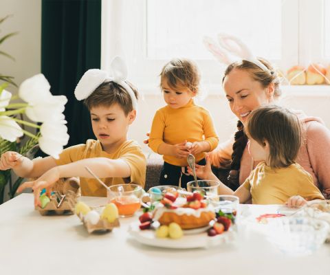Madre con tre bambini piccoli intorno al tavolo dipingono le uova di Pasqua