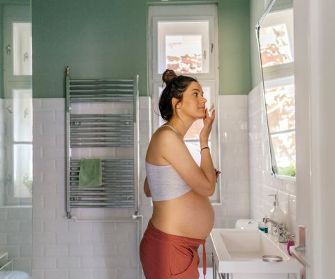 Schwangere steht in einem Badezimmer und cremt sich das Gesicht ein