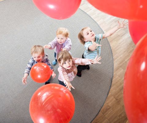 Kleinkinder spielen mit roten Luftballons