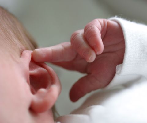 Un bebè si tocca l'orecchio con la mano