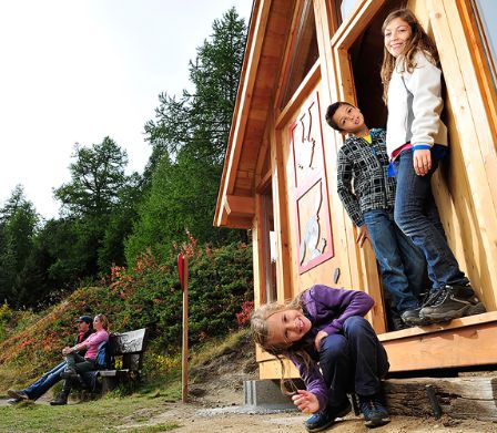 Famiglia durante un’escursione, i bambini sono davanti a una casa di tronchi
