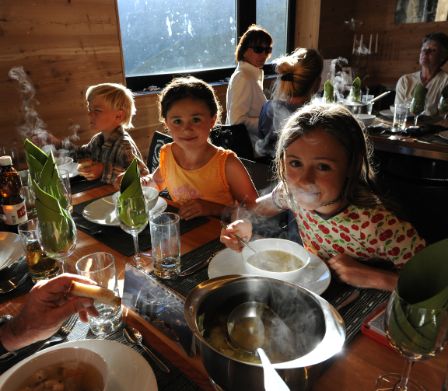 Famiglia seduta al tavolo ben apparecchiato di una capanna mangia una zuppa fumante