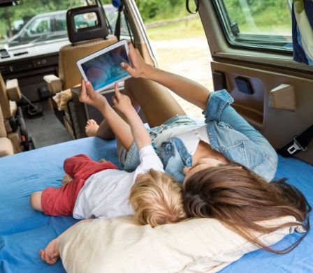 Mutter und kleines Kind liegen im Auto mit einem Tablet-PC